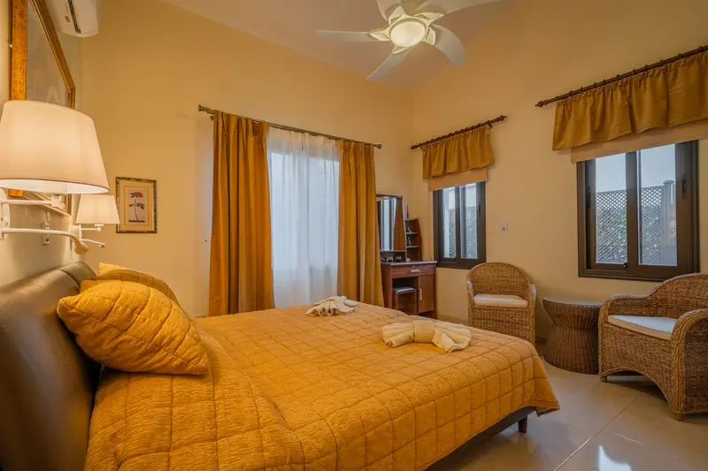 Gold bedroom with king size bed, ceiling fan, dedicated AC/heating unit, vanity, large built-in wardrobes, bluetooth speaker/alarm clock, and seating group. Views of the garden. Ensuite bathroom with bath tub/shower combo.