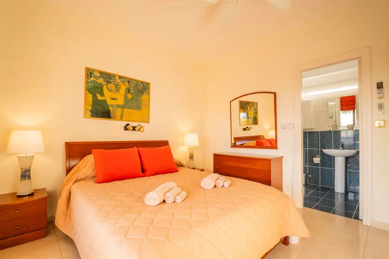 Master bedroom featuring a private balcony with stunning views of the Mediterranean and a full ensuite bath with a walk-in shower. The room has spacious closets, a ceiling fan, a dedicated AC/heating unit, and a Bluetooth-enabled speaker/alarm clock combo.